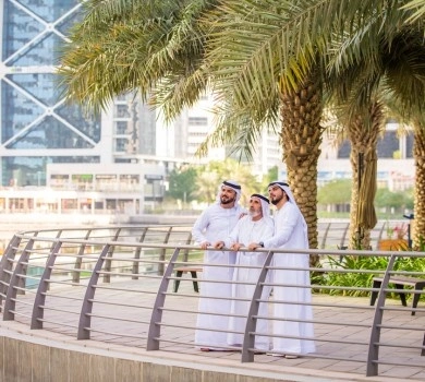 emirati men walking along dubai marina promenade with palm trees