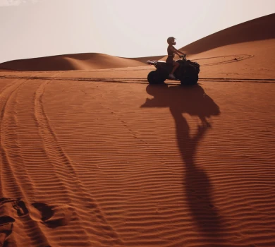 person riding quad bike across red sand dunes in desert