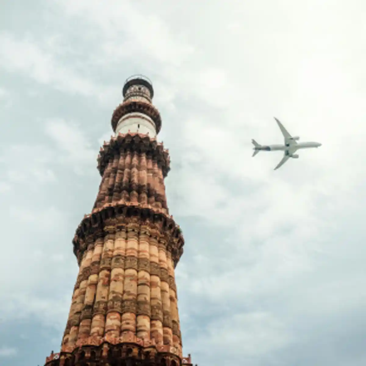 Qutub Minar tower with airplane flying overhead in Delhi