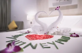 Romantic honeymoon hotel room with towel swans, rose petals and welcome decoration on bed