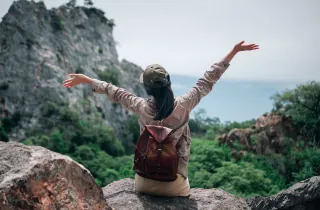 Traveller sitting on rock with arms raised overlooking Sri Lanka mountains and valley