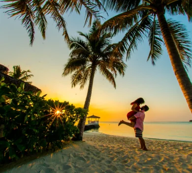 romantic-beach-sunset-couple Alt: Couple embracing on tropical beach at sunset with palm trees
