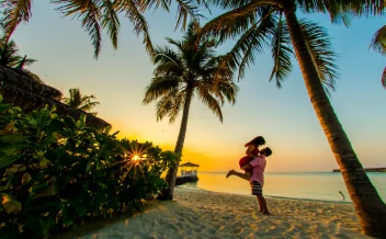 romantic-beach-sunset-couple Alt: Couple embracing on tropical beach at sunset with palm trees