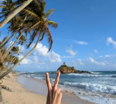 Hand showing peace sign on tropical beach with palm trees
